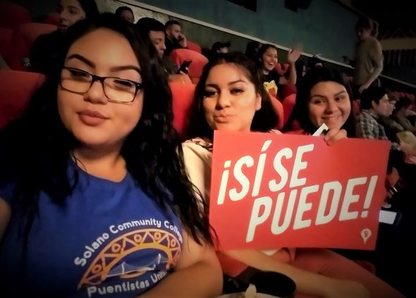 Three Puentistas Listening to Dolores Huerta holding a sign that says si se puede.