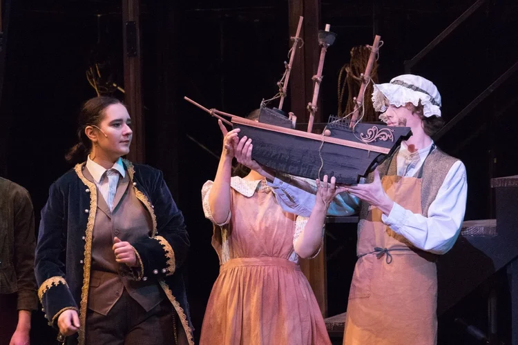 Three people in costume holding a model ship