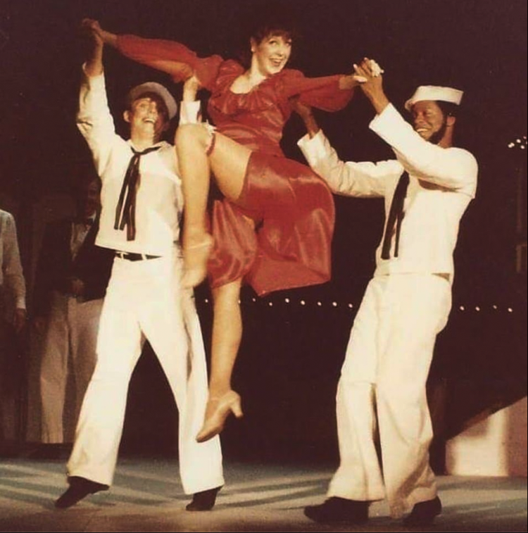 Two people in sailor costumes holding up a woman in red dress